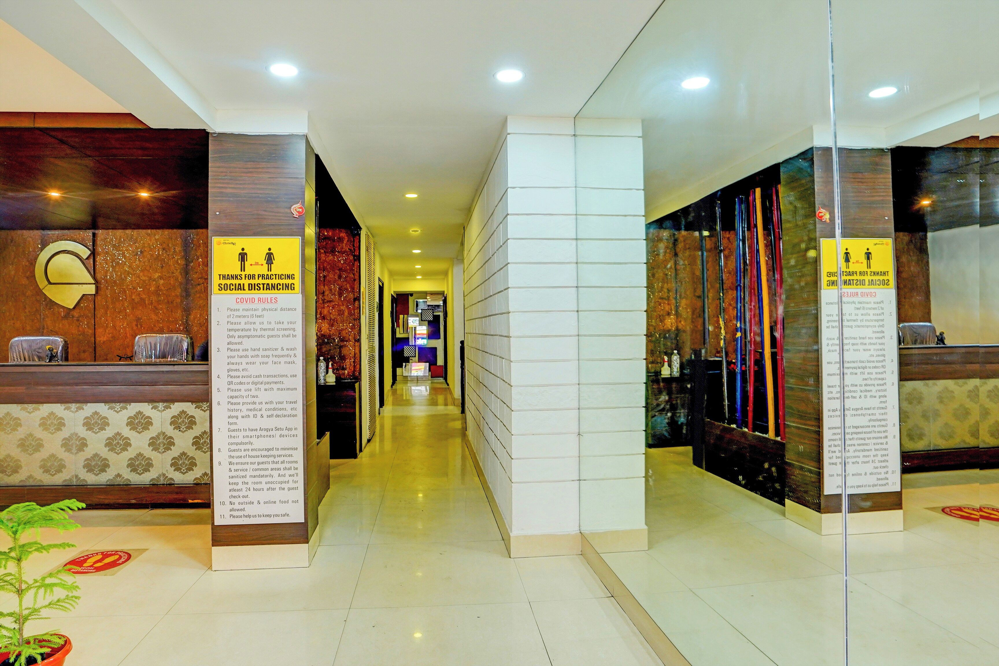 Zona de recepción de hotel con un cartel claro que detalla las normas de COVID-19, un mostrador de recepción y un pasillo que conduce a otras áreas.