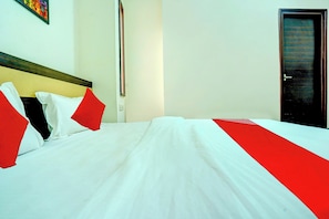 A hotel room with a neatly made bed, a door, and a wall with a painting. - Super Hotel O Sunshin Deluxe (Nagpur)