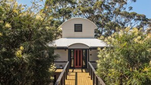 A building with a curved roof and a red door, surrounded by dense greenery. - Bangalay on Tallwood (Mollymook Beach)