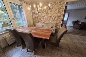 A dining area with a wooden table, chairs, a chandelier, and a floral wallpaper backdrop. - Holiday apartment with 1 bedroom (Butjadingen)