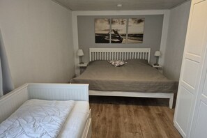 A bedroom with a bed, a smaller bed or sofa, a nightstand, a lamp, and a wall-mounted picture. - Holiday apartment with 1 bedroom (Butjadingen)