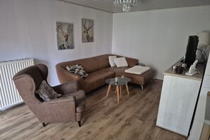 A living room with a brown sofa, a brown armchair, a small round coffee table, and a white cabinet. - Holiday apartment with 1 bedroom (Butjadingen)