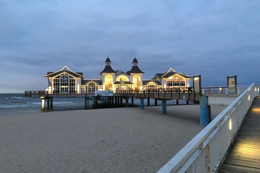 A beachfront hotel with a pier extending into the sea, featuring multiple levels and a prominent central tower.