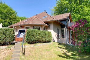 Ein zweistöckiges Haus mit geneigtem Dach, einem sichtbaren Schornstein und einer Veranda mit einer Bank.