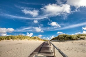 A wooden boardwalk leading through a sandy beach area with dunes on either side. - Apartment in Juist with swimming pool (Juist)
