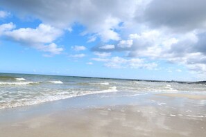 Una platja amb onades, cel clar i un moll que s'endinsa a l'aigua.
