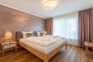A bedroom with a wooden bed, bedside tables, a lamp, and a window with curtains. - Holiday apartment with 1 bedroom (Lohme OT Ranzow)
