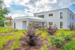 A modern two-story house with a flat roof, large windows, and a well-maintained garden with various plants and shrubs. - Holiday apartment with 1 bedroom (Lohme OT Ranzow)
