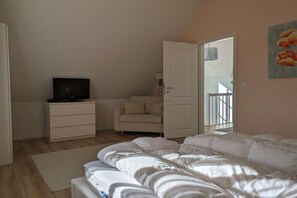 Ein Schlafzimmer mit einem Bett, einem Fernseher auf einer Kommode, einem Sessel und einer Tür, die auf einen Balkon führt.