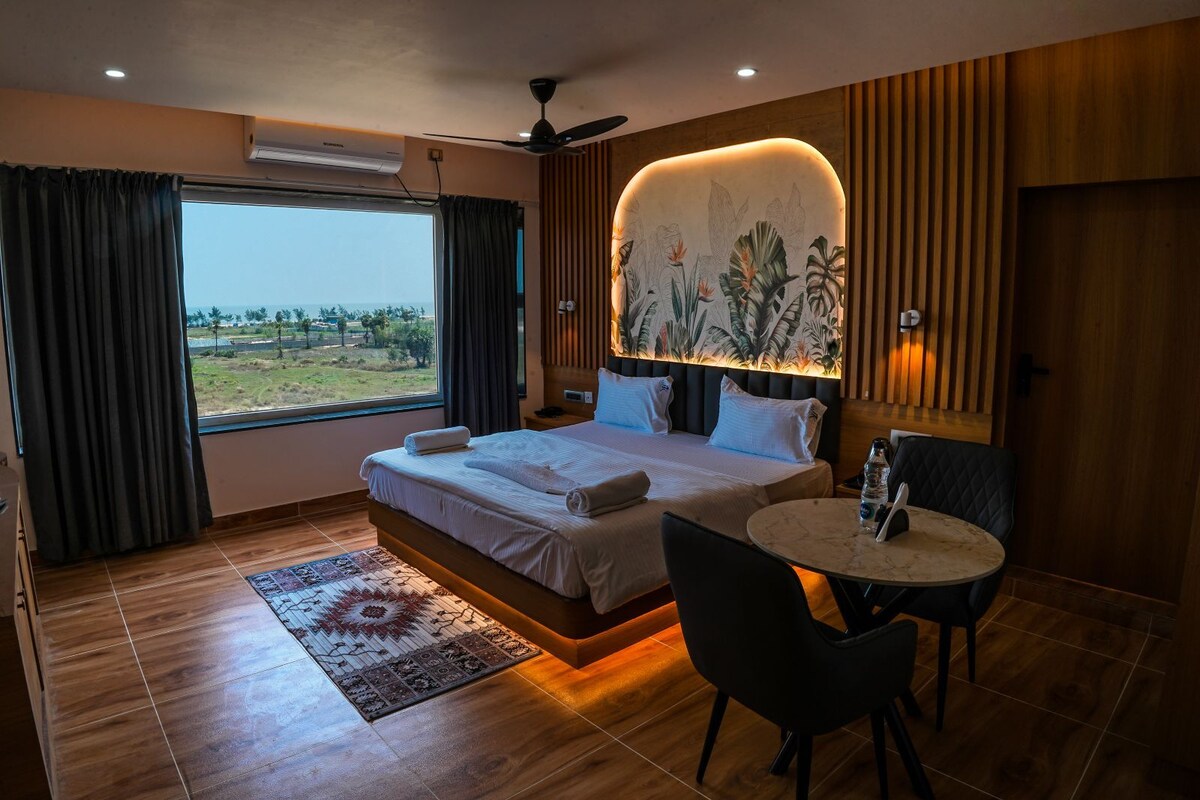 A hotel room with a bed, a small table, a chair, a view of the outdoors, and a ceiling fan.