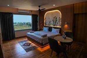 A hotel room with a bed, a small table, a chair, a view of the outdoors, and a ceiling fan. - Hotel JK PARADISE (Chirala)