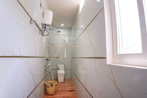 A narrow bathroom with a shower, toilet, and a window providing natural light. - Hotel JK PARADISE (Chirala)