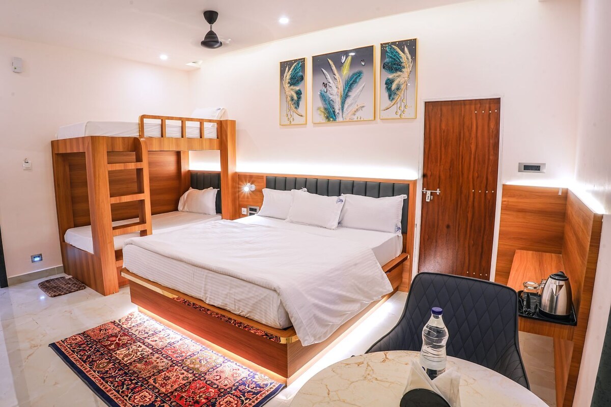 A hotel room with a large bed, a wardrobe, a desk with a chair, and a small table with a water bottle.