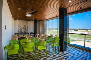 A room with a view of a golf course, wooden ceiling, and green chairs. - Hotel JK PARADISE (Chirala)