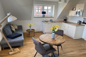 A modern living space with a sofa, a dining table, and a kitchen area. - Holiday apartment with 1 bedroom (Baltrum)
