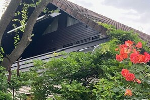 A building with a sloped roof and a tree in the foreground. - Holiday apartment Höflich "Heide 1" (Bad Zwischenahn)