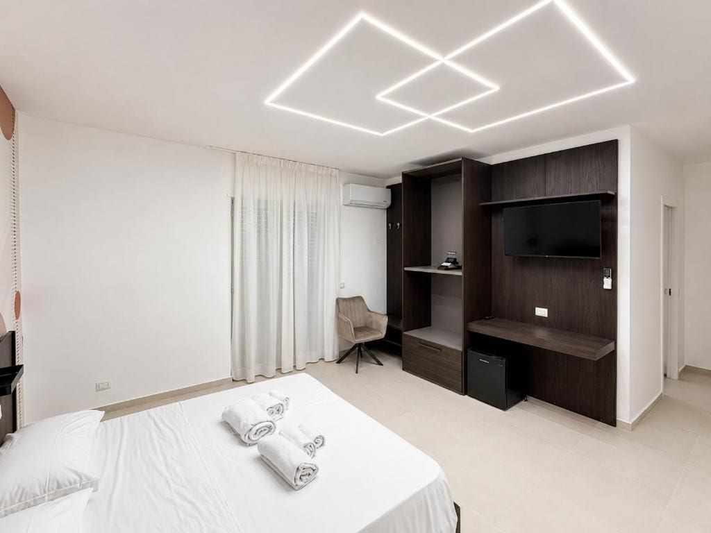 Ein modernes Hotelzimmer mit einem großen Bett, einem Flachbildfernseher, Einbauschränken und einem Sessel.