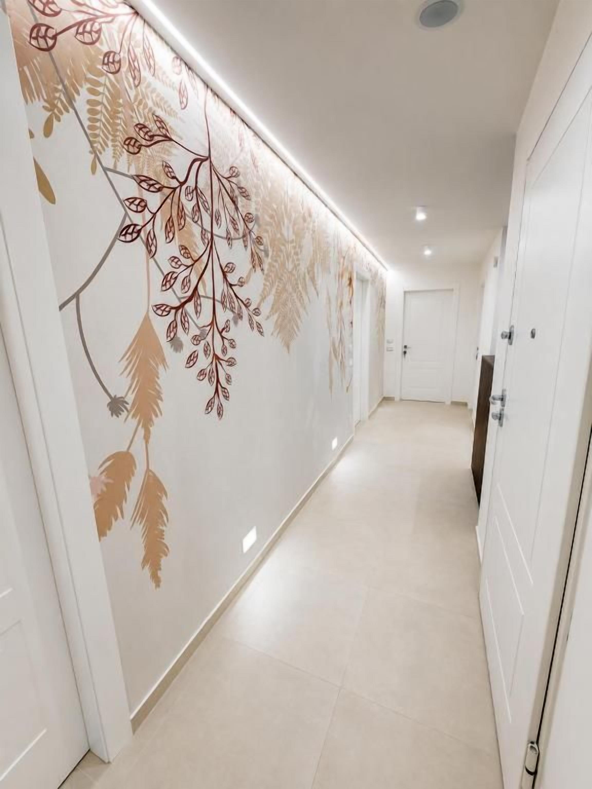 A hallway with a decorative wall featuring leaf patterns, a door on the right, and a light fixture on the ceiling.