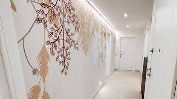 A hallway with a decorative wall featuring leaf patterns, a door on the right, and a light fixture on the ceiling.