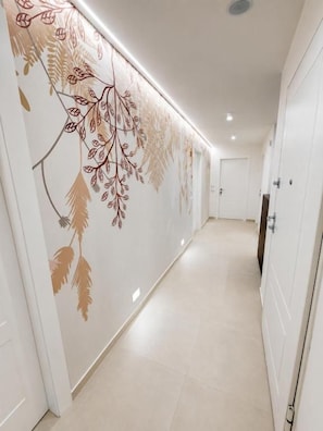 A hallway with a decorative wall featuring leaf patterns, a door on the right, and a light fixture on the ceiling. - Emma's Rooms (Tropea)