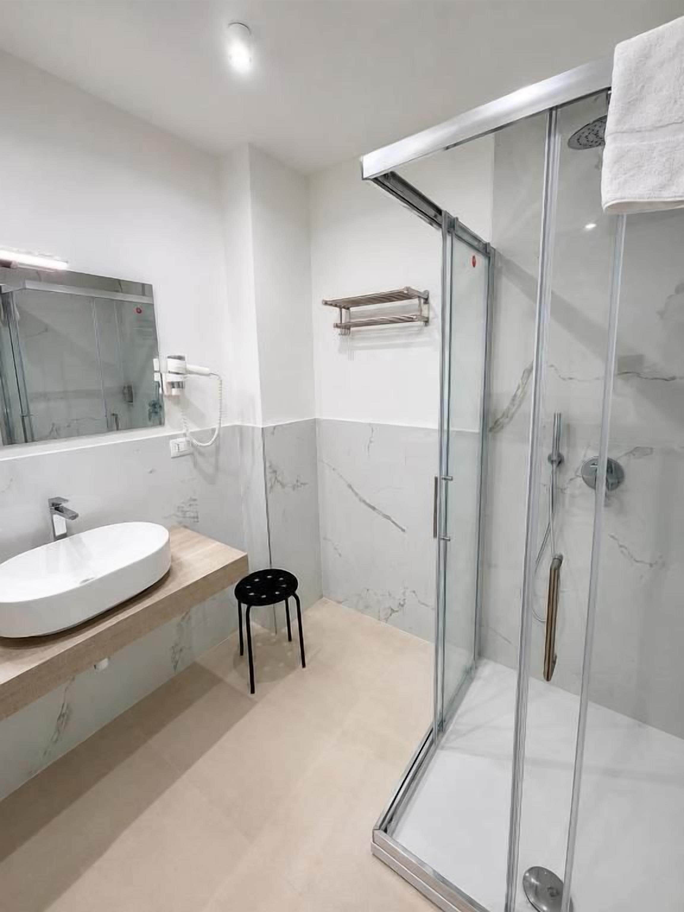 Une salle de bain moderne avec une douche à parois de verre, un lavabo rond et un petit tabouret.