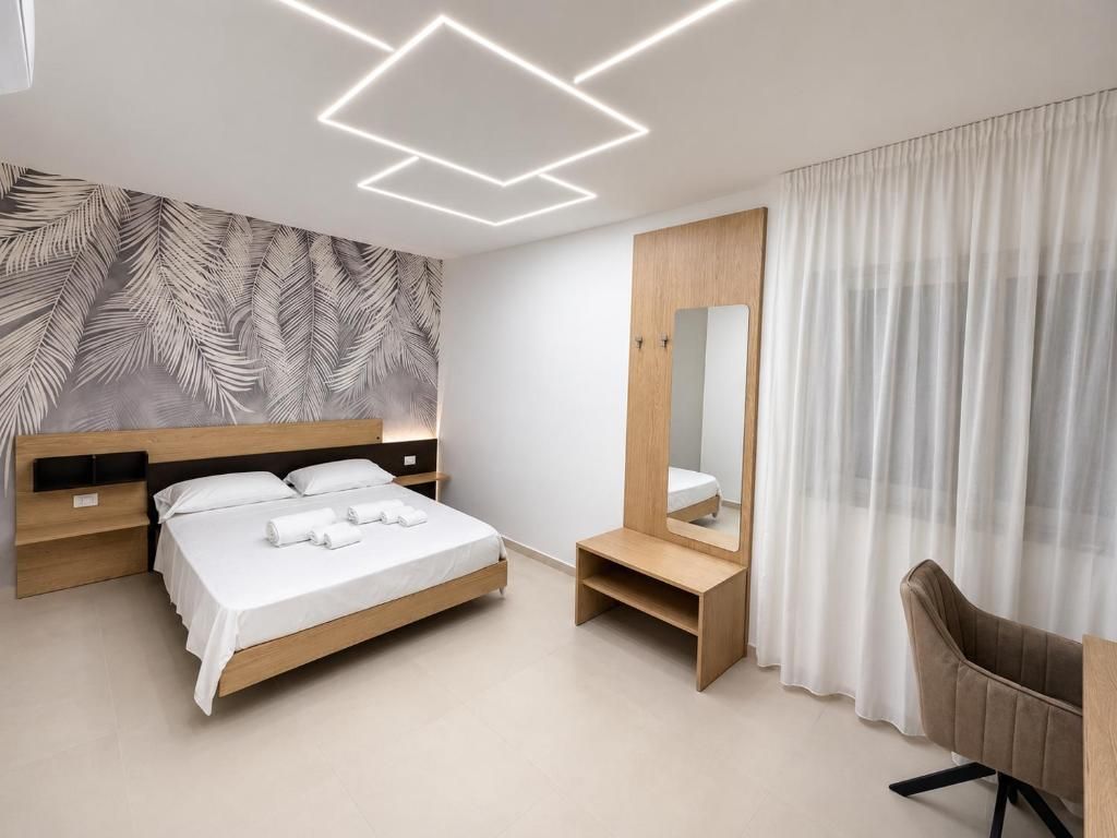 A modern bedroom with a bed, bedside tables, a mirror, a chair, and a wall with leaf patterns.