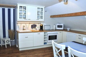 A compact kitchen with white cabinetry, a wooden countertop, a small dining table, and a hanging pot rack. - Linden holiday apartment with balcony (Borkum)