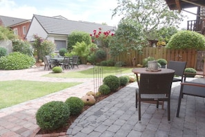 A patio area with a round table and chairs, surrounded by a brick pathway and small bushes. - Linden holiday apartment with balcony (Borkum)