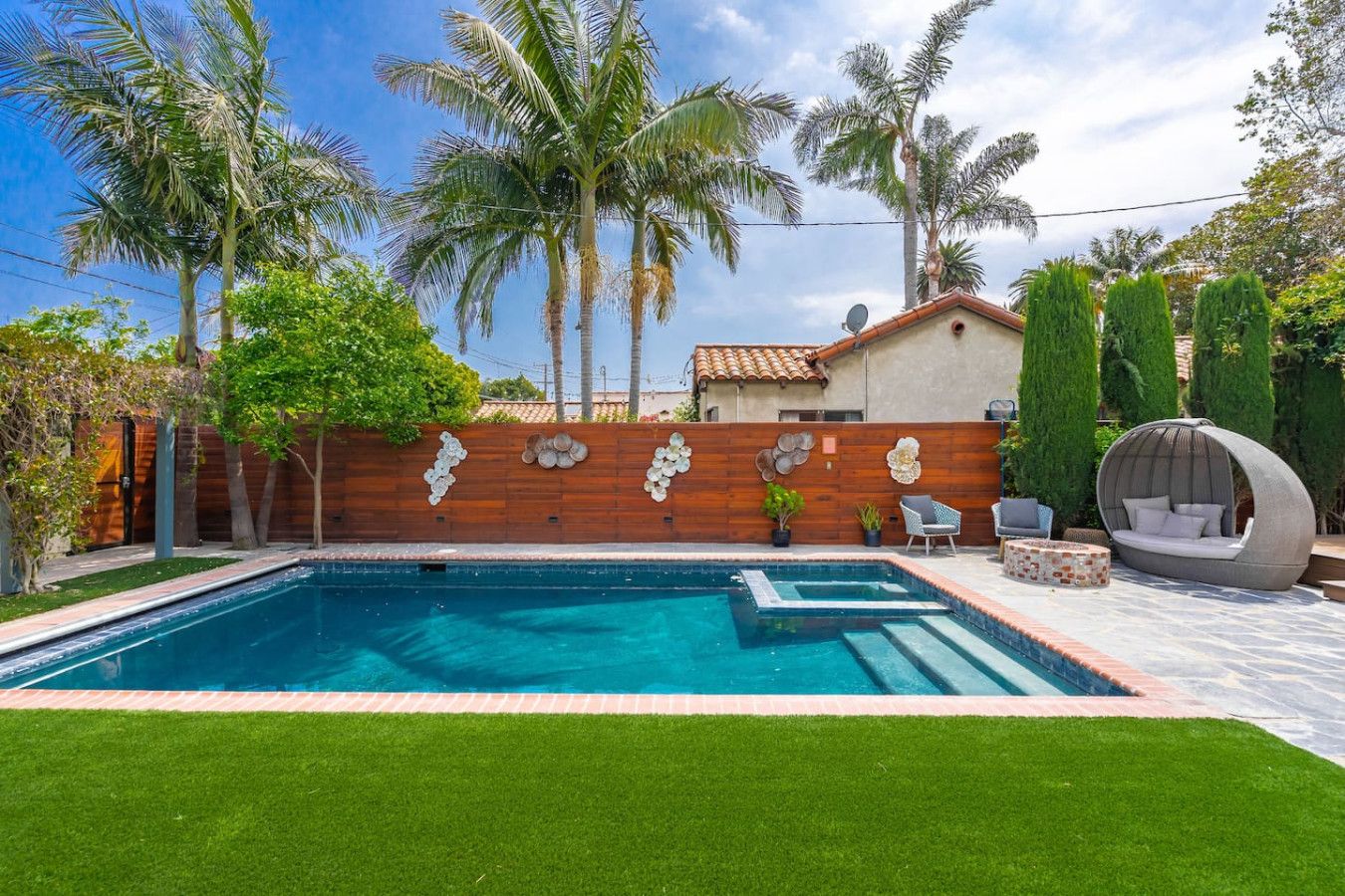 A swimming pool with a wooden deck, surrounded by palm trees and a well-maintained lawn.
