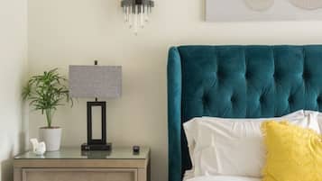 A bedroom with a bed, a nightstand, a lamp, a potted plant, and a wall art piece.