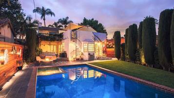 A residential property with a swimming pool, a covered outdoor seating area, and a staircase leading to a second floor.