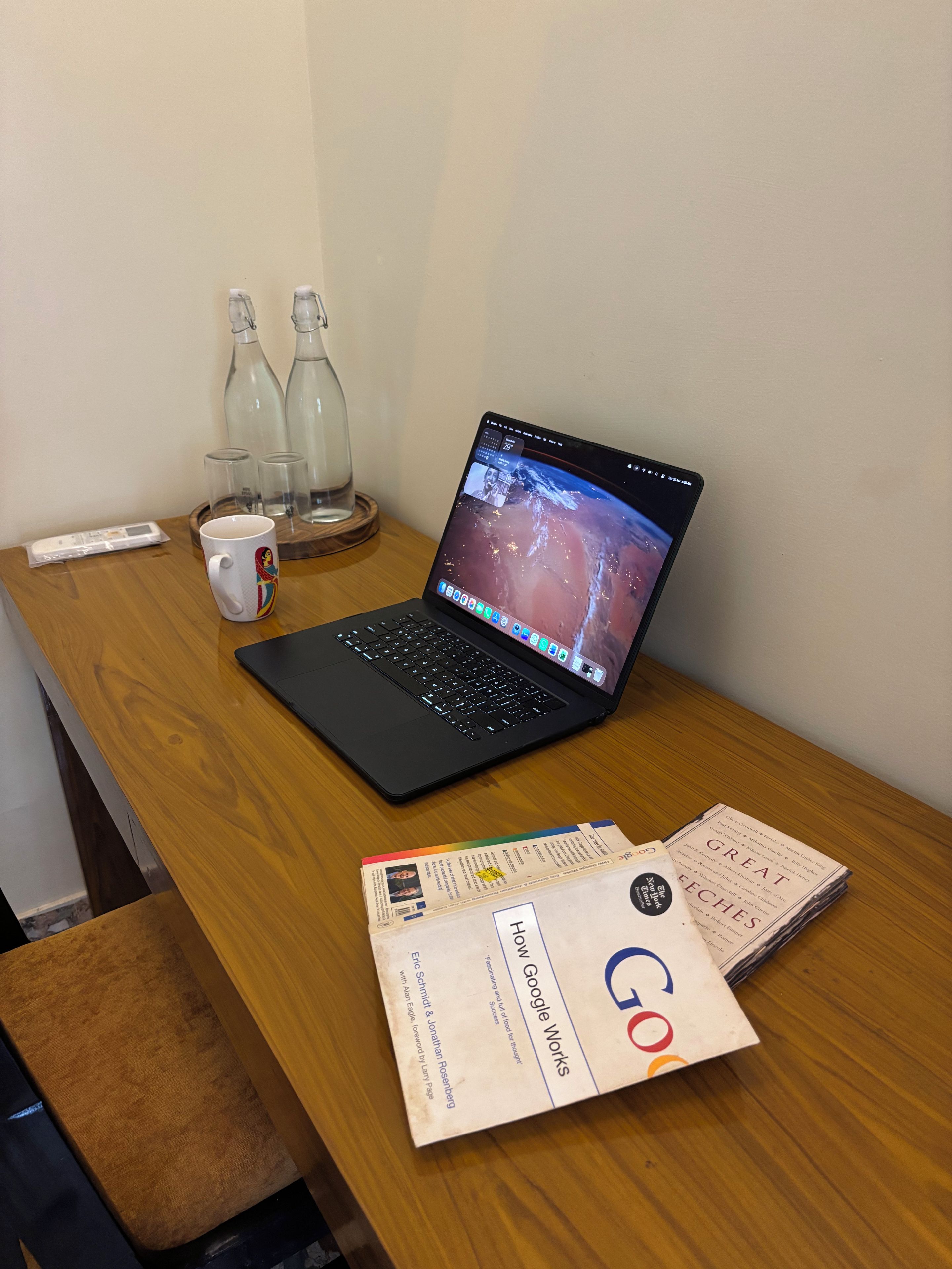 A laptop on a wooden desk with a book titled 'Google Works' and a mug.