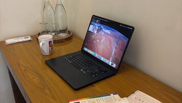 A laptop on a wooden desk with a book titled 'Google Works' and a mug.