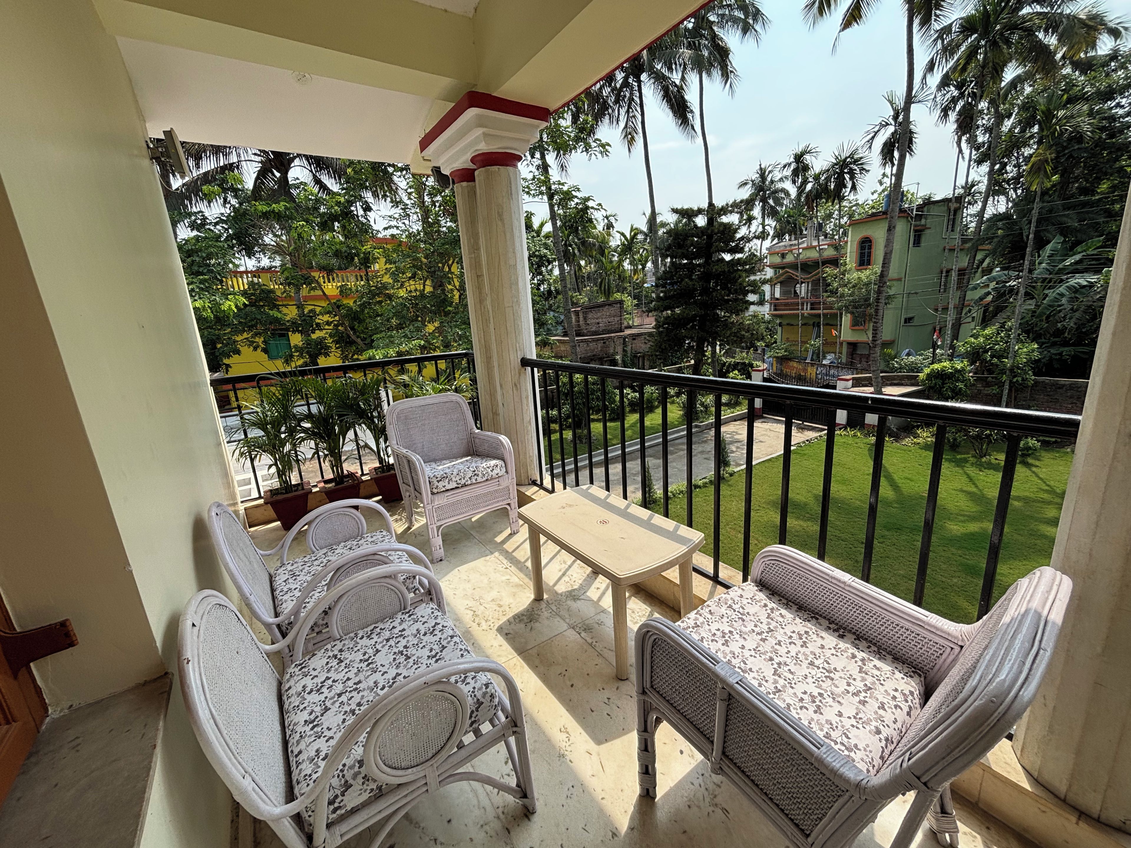 A balcony with wicker furniture, a small table, and a view of a green lawn and buildings.