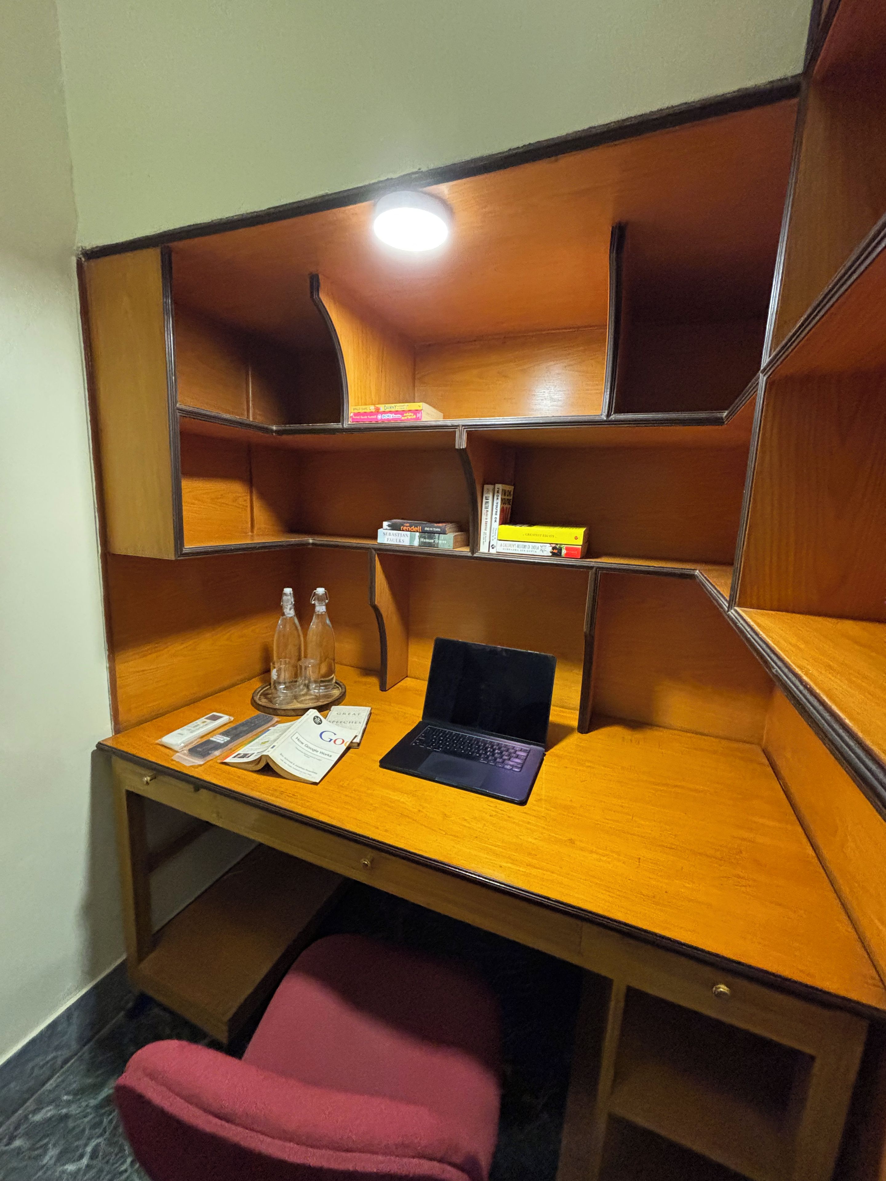 A wooden desk with a laptop, a glass bottle, and some papers.