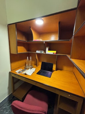 A wooden desk with a laptop, a glass bottle, and some papers.