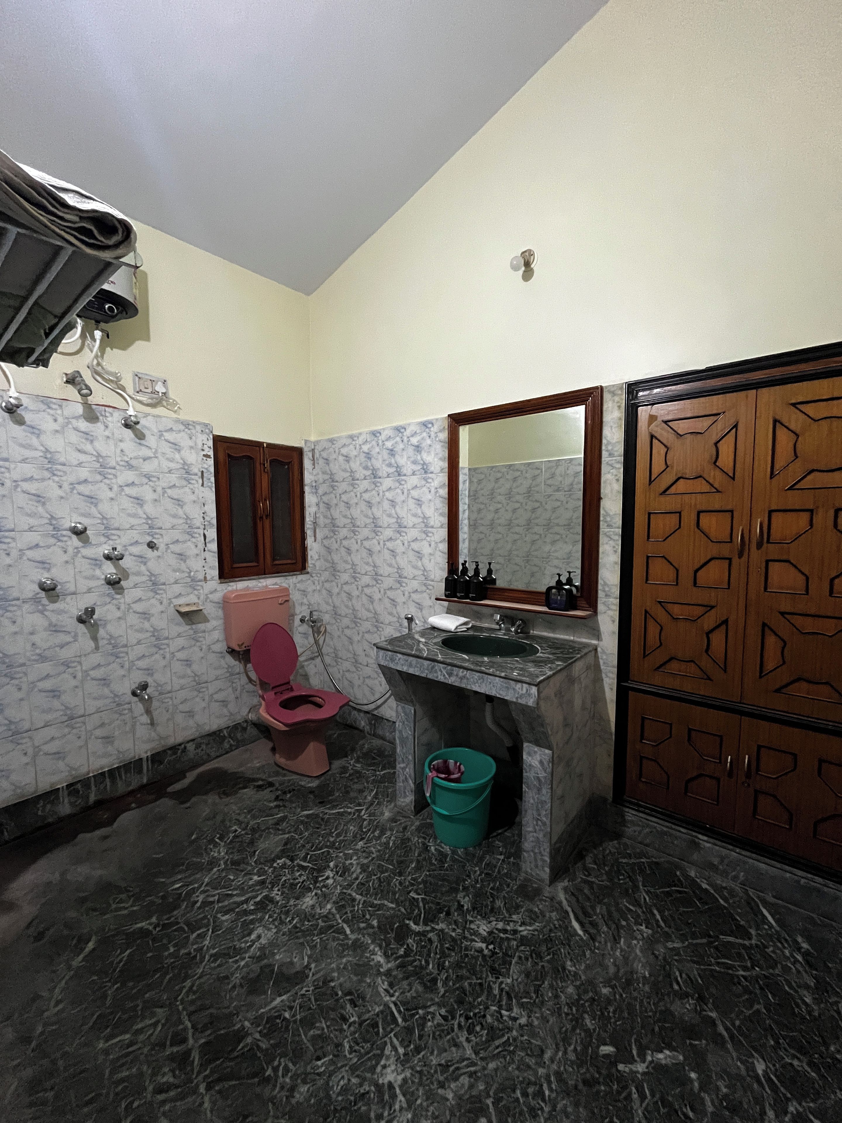 A bathroom with a pink toilet, a sink with a mirror, and a wooden cabinet with geometric patterns.