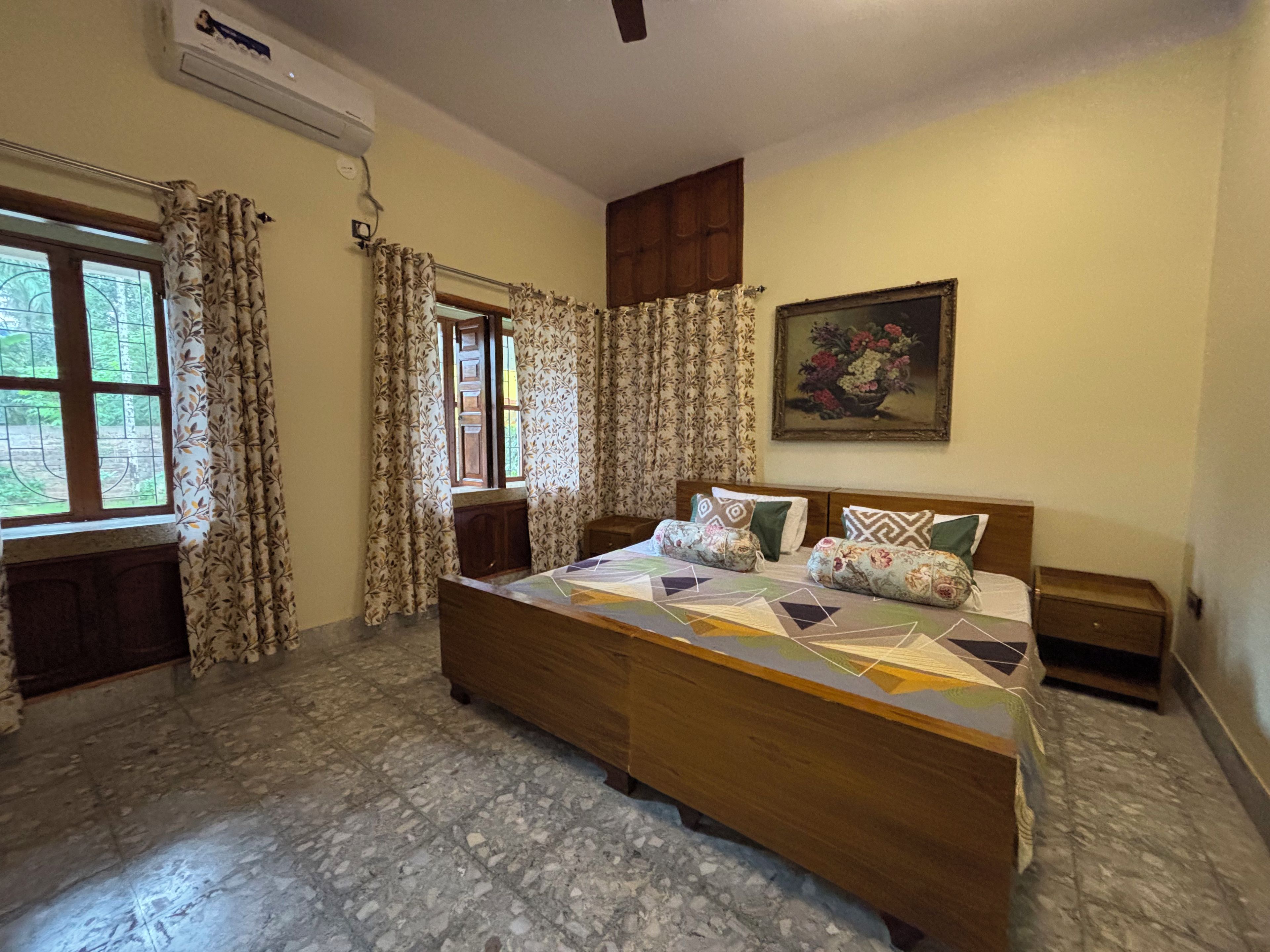 A bedroom with a wooden bed, a nightstand, a wall-mounted air conditioner, and a window with curtains.