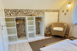 A bedroom with a bed, a wicker chair, a wardrobe with shelves, and a wall with a log pattern. - Holiday home with 3 bedrooms (Plau am See)