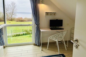 A room with a desk, chair, and a television. There is a window with curtains, a view of the outdoors, and a door with a handle. - Holiday home with 3 bedrooms (Plau am See)