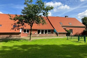 A building with a red-tiled roof, a brick facade, and a green lawn. - Bruns holiday apartment (Ihlow)
