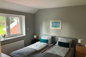 A bedroom with two beds, a window with a view of a brick building, a framed picture on the wall, and bedside lamps. - Bruns holiday apartment (Ihlow)