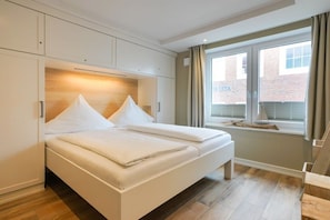 A bedroom with a bed, built-in wardrobe, and a window with a view of a brick building. - wat"nmeer im Achthus auf Juist (Juist)