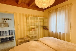 A room with a bed, a wooden bench, a white shelving unit, and a window with curtains. - Holiday home with 3 bedrooms (Plau am See)