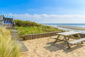 Een houten constructie aan het strand met een geribbelde luifel, een picknicktafel en een steeg die naar het strand leidt.