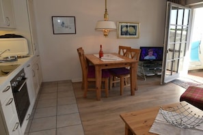 A compact kitchen with a dining table and chairs, a television, and a door leading to an outdoor area. - Holiday apartment in Sylt with 1 bedroom (Wenningstedt)