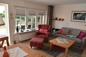A living room with a plaid armchair, a grey sofa, a wooden coffee table, and a window with blinds. - Holiday apartment in Sylt with 1 bedroom (Wenningstedt)