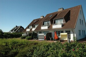 A two-story house with a sloped roof, a balcony, and a garden area with plants and outdoor furniture. - Holiday apartment in Sylt with 1 bedroom (Wenningstedt)
