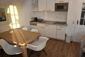 Eine kleine Küche mit weißen Schränken, einer Mikrowelle, einem Spülbecken und einem Essbereich mit einem Holztisch und weißen Stühlen.