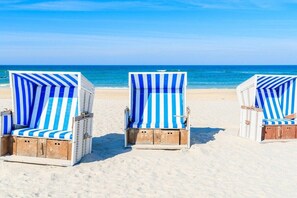 Three beach chairs with blue and white stripes, positioned on a sandy beach with the ocean in the background. - Arnika Hof Holiday Apartment 15 (Wenningstedt)